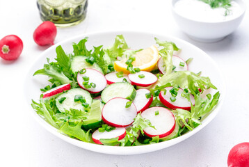 Fresh summer salad with radishes, cucumbers, lettuce and green onions with greek yogurt dressing, white table background, top view