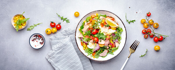 Canned tuna salad with cherry tomatoes, red onion, eggs, sweet corn, paprika, lettuce, radicchio and arugula. Gray table background, top view banner