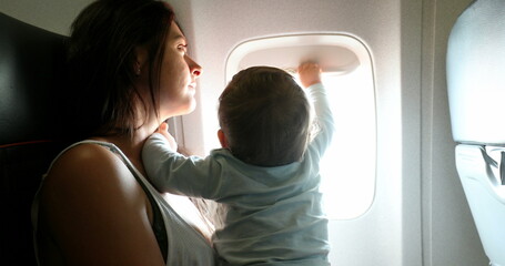 Baby reaching out to plane window. Mother traveling with infant son child