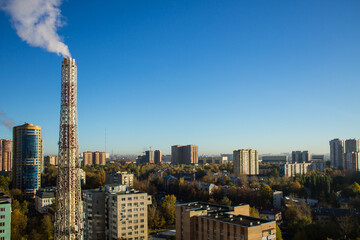 Urban industrial landscape - modern multi-storey houses among green trees and a metal pipe of a thermal power plant against a blue sky and copy space