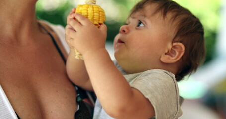 Adorable baby toddler holding corn cob offering to mother