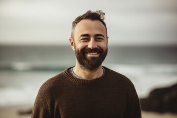 Fototapeta premium Portrait of handsome bearded man smiling at camera while standing on beach