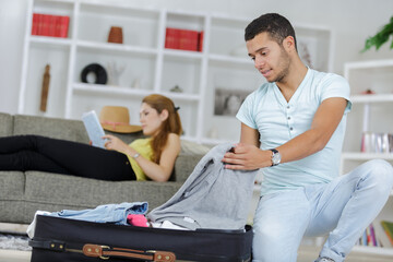 Fototapeta premium man packing suitcase while lady reads on the sofa