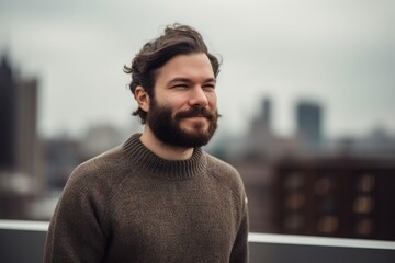Fototapeta premium Young handsome bearded hipster man with long hair in a brown sweater posing in an urban context