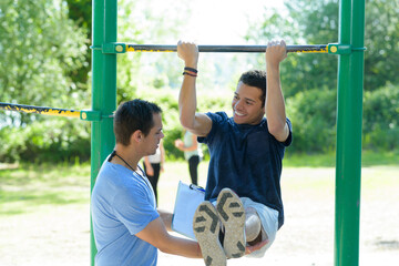 Naklejka premium young man with trainer doing leg raises outdoors