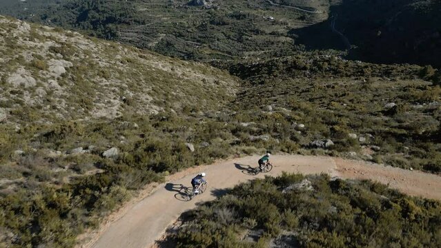 Group of gravel cyclists descend a gravel serpentine road in a mountains. Cycling in Spain Costa Blanca concept video. Aerial drone footage in slow motion. Camera revealing breathtaking mountain view.