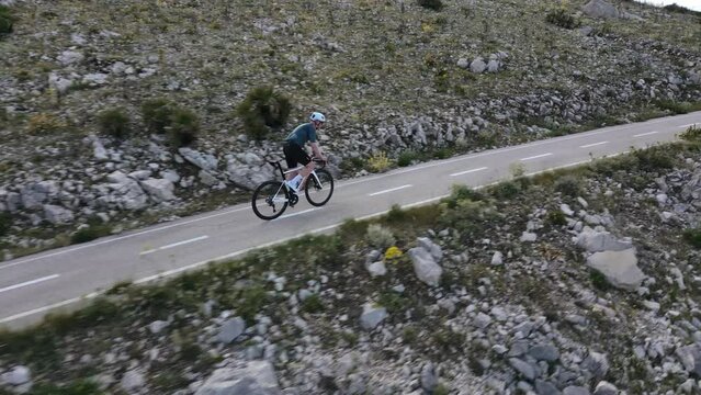 Dedicated road cyclist takes on the challenging uphill climb of a rural road in the Spanish mountains. Intense uphill training session in slow motion. Pushing to the limit concept. Cycling holiday.