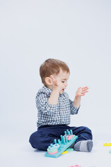 A cute little boy in a checkered shirt sits on a white background and plays with wooden educational toys. Ecological wooden toys for children