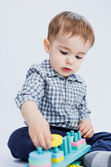 A little boy in a shirt is building a colorful wooden toy on a white background. The concept of children's development, games for children, toys. Copy space