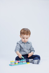 A little boy in a shirt is building a colorful wooden toy on a white background. The concept of children's development, games for children, toys. Copy space