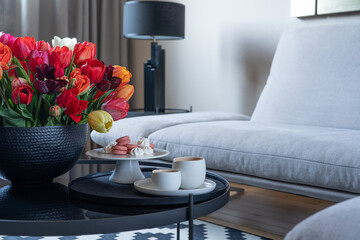 Modern home interior. Comfortable grey sofa, gorgeous flowers in a vase, covered coffee table with...