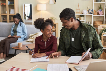 Military dad helping his daughter with her homework while they sitting at table in the living room