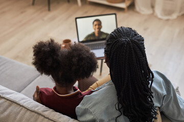 Rear view of family having video call with their dad on laptop, they sitting on sofa and talking to him