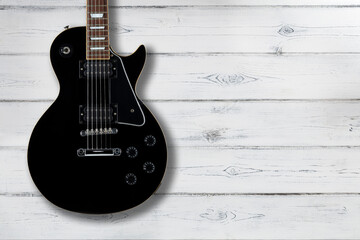Obraz premium Black electric guitar on a distressed white wooden background