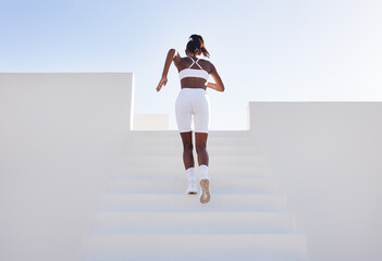 Back view of a woman in white sportswear running up on stairs. Rear view of a young female jogger exercising in a white outdoor studio. - obrazy, fototapety, plakaty
