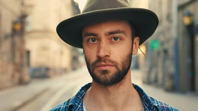 Close Up of Millennial Handsome Man in Hat Looking to Camera. Portrait of Good Looking Guy Standing at Old City Street. Tourist in the City. Concept of People and Real Life.