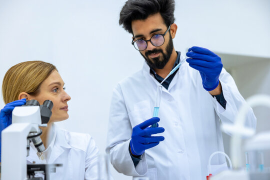 Young female and male scientists using pipette with test tube in medical science laboratory.
