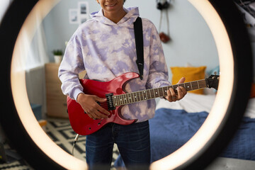 Cropped shot of happy teenage guy with electric guitar standing behind round frame for video...