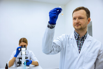 Male scientist analyzes liquid female researcherworking with microscope investigating medical sample