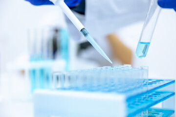 Unrecognizable scientist dripping blue liquid from pipette into test tube at table in laboratory.