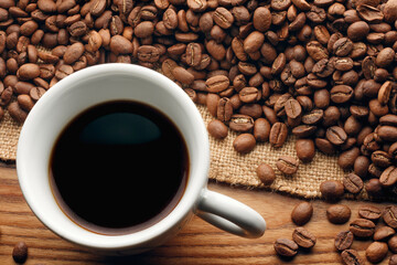 Cup black coffee. Roasted beans on sack on wooden table.