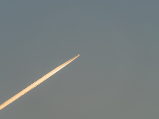 The plane flies in the blue sky and leaves a bright trail