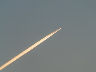 The plane flies in the blue sky and leaves a bright trail