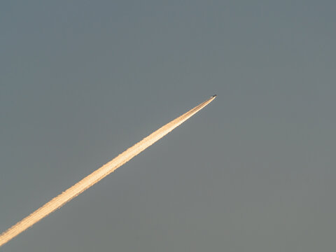 The plane flies in the blue sky and leaves a bright trail