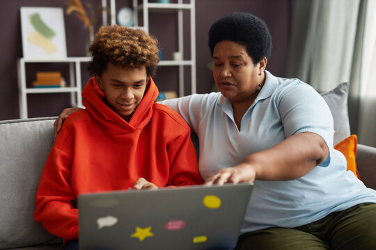 African American mature woman and diligent teenage boy looking at laptop screen while watching online video or discussing information