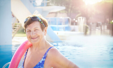 Active senior (elderly) woman (over age of 50) in sport goggles, swimsuit and with swim noodles...