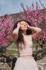 A young girl among beautiful peach flowers in full bloom. Pink peach blossom garden. Springtime.