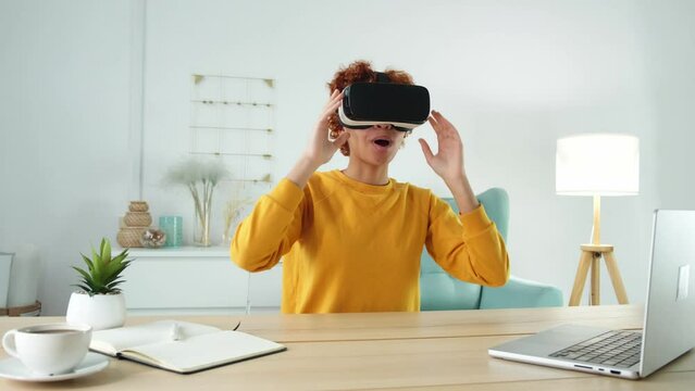African american young woman wearing using virtual reality metaverse VR glasses headset at home. Girl puts on virtual reality helmet. Technology simulation hi-tech videogame concept