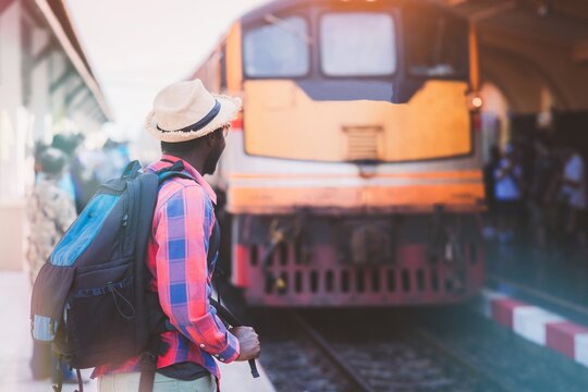 African man traveling with backpack in train, backpack and hat at train station with travelers, travel concept. Travel man walking at train station