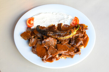Traditional turkish iskender kebab in copper plate with yogurt, grilled tomatoes and fresh vegetables.