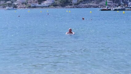 happy mature man, healthy senior 60 years old swims in open water, sea, ocean, river, in sea harbor port of Soller, frolic, playing in water, improve health, concept learning swimming skills