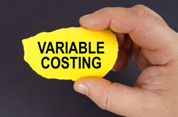 On a black background, in the hands of a man, a yellow torn cardboard with the inscription - Variable Costing