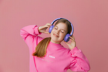 Photo of a cute funny young teenage girl in a pink jumper, headphones, dancing, enjoying music on a background