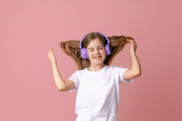 Fototapeta na wymiar Photo of a cute funny young teenage girl in a pink jumper, headphones, dancing, enjoying music on a background