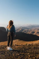Papier Peint photo Lavable les îles Canaries young woman with flowing hair and urban outfit walking at sunset looking at the desert on the volcanic island of fuerteventura