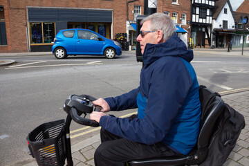 Close up shot of man on mobility scooter waiting to cross a main road while cars drive passed, enjoying the freedom that his disabled scooter gives him to get out and about despite his disability.