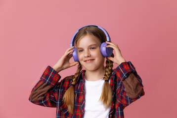 Photo of a cute funny young teenage girl in a pink jumper, headphones, dancing, enjoying music on a background