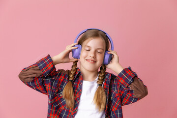 Photo of a cute funny young teenage girl in a pink jumper, headphones, dancing, enjoying music on a background