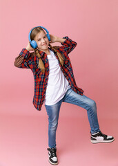 Photo of a cute funny young teenage girl in a pink jumper, headphones, dancing, enjoying music on a background