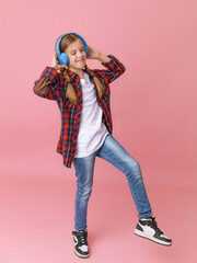 Photo of a cute funny young teenage girl in a pink jumper, headphones, dancing, enjoying music on a background
