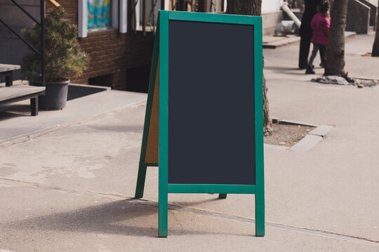 Blackboard in front of restaurant entrance. Mock up menu blank board sign stand near shop or cafe restaurant. Street magnetic sidewalk chalkboard