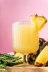 a glass of pineapple juice and a pineapple on wooden tray