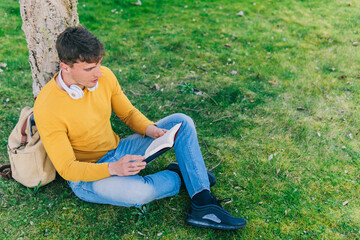 Man reading book in park. High angle side view of young man and woman reading book while sitting on grass in park