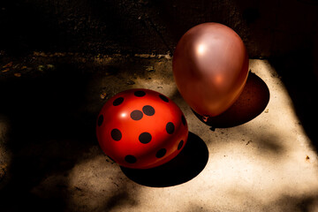 Close-up of red with black polka dots and pink balloons on a wet concrete garage floor. Moldy tan walls and rays of sun.
