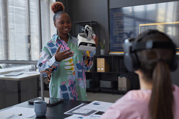 African American programmer presenting new VR glasses to her colleagues and they testing them during meeting in office