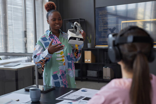 African American programmer presenting new VR glasses to her colleagues and they testing them during meeting in office